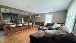 A modern living room with a brown sofa, white cushions, and a wooden floor. - Charming 4-bedroom house with a big yard in Poultney (Poultney)