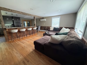 A modern living room with a brown sofa, white cushions, and a wooden floor.