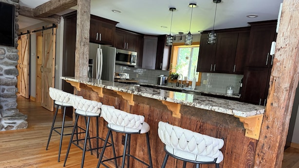 A kitchen with a marble countertop, wooden bar stools, and dark cabinets. - Charming 4-bedroom house with a big yard in Poultney (Poultney)