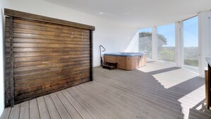 Ein geräumiger Balkon mit Whirlpool, Holzboden und großen Fenstern mit Blick ins Freie.