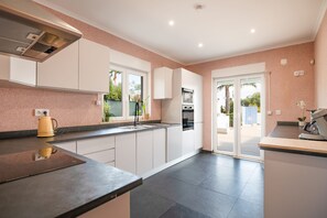 A modern kitchen with white cabinets, a built-in oven, and a large window. - Your private retreat with garden, terraces, and stunning sunset views. (Estoi)