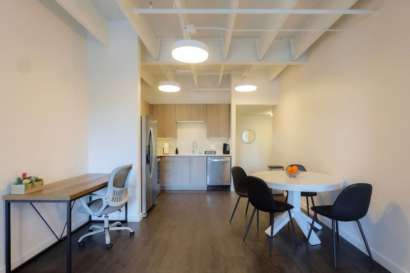 A modern kitchen with a dining area, featuring a wooden table, chairs, and a refrigerator.
