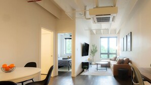 A modern living room with a dining area, a sofa, a TV, and a large window. - Above The Roots - Stylish Square (Washington)