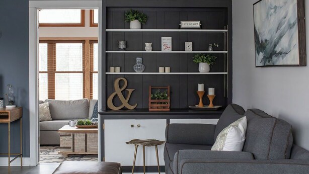 En moderne stue med en grå sofa, et sofabord og en reol med dekorative genstande.