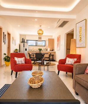 Uma sala de estar moderna com sofás vermelhos, uma mesa de centro e uma área de jantar ao fundo.