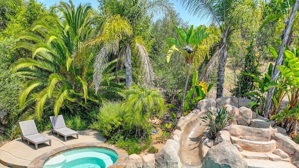Una piscina con cascada de roca natural, rodeada de abundante vegetación y dos sillones de descanso.