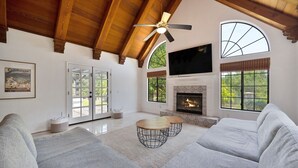Amplia sala de estar con chimenea, asientos cómodos y ventanas grandes que ofrecen vistas al exterior.