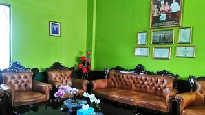 A room with a green wall, a brown leather sofa, a glass coffee table with flowers, and framed certificates on the wall. - Hotel Antik (Soreang)