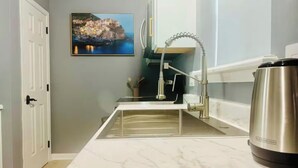 Eine Küche mit weißer Marmorarbeitsplatte, einem Edelstahlkocher, einem Wasserhahn und einem gerahmten Bild an der Wand.