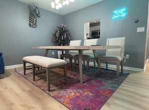 Un espace repas comprenant une table et des chaises, un banc, une décoration murale à motifs zébrés, un néon et une plante en pot.