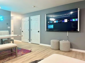 Un salon moderne avec un téléviseur à écran plat fixé au mur, une table à manger, deux portes et un banc.