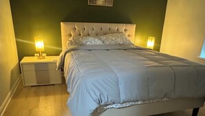 Ein Schlafzimmer mit einer gesteppten Kopfteile, einem Bett mit weißer Bettdecke, zwei Nachttischlampen und einem gerahmten Bild an der Wand.