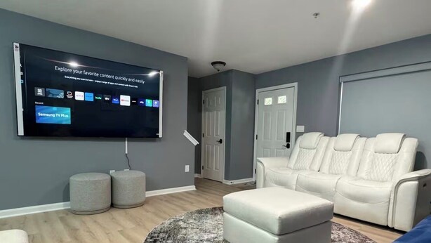 Ein modernes Wohnzimmer mit Flachbildfernseher, einer weißen Ledersofa, einem blauen Sofa und einem gemusterten Teppich.