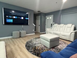 Un soggiorno moderno con televisore a schermo piatto, un divano in pelle bianca, un divano blu e un tappeto decorato.