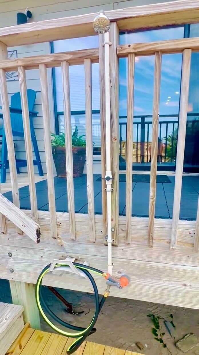 A wooden deck with a metal railing, a hose, and a water spout.