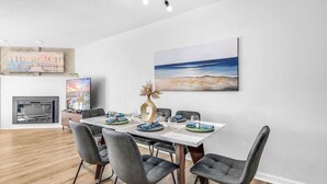 Zona pranzo con tavolo bianco, sedie grigie e un quadro raffigurante una spiaggia.