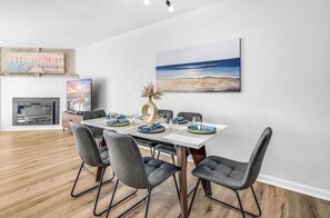 A dining area with a white table, grey chairs, and a painting of a beach scene. - Steps to the Beach|Pool & Gulf Views| sleeps 6 (Saint George Island)