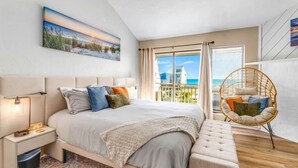 Una camera da letto con un letto, comodini, una sedia sospesa e un'ampia finestra vista mare.