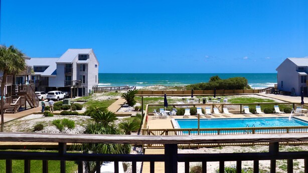 Una proprietà fronte spiaggia con piscina, sdraio e vista sull'oceano.