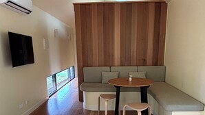 Una sala de estar moderna con piso de madera, un ventilador de techo, un banco empotrado con cojines y una mesa redonda con dos taburetes.