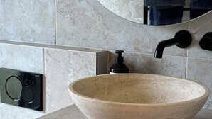 Un baño con un lavamanos grande, redondo y de cerámica color beige, un grifo negro y un espejo encima.