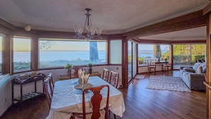 A spacious dining area with a view of the sea, wooden flooring, and a chandelier. - The Seagates Private Coastal Retreat | Coos Bay (Coos Bay)