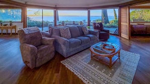 A spacious living room with a grey sofa, a wooden coffee table, and a view of the ocean through large windows. - The Seagates Private Coastal Retreat | Coos Bay (Coos Bay)