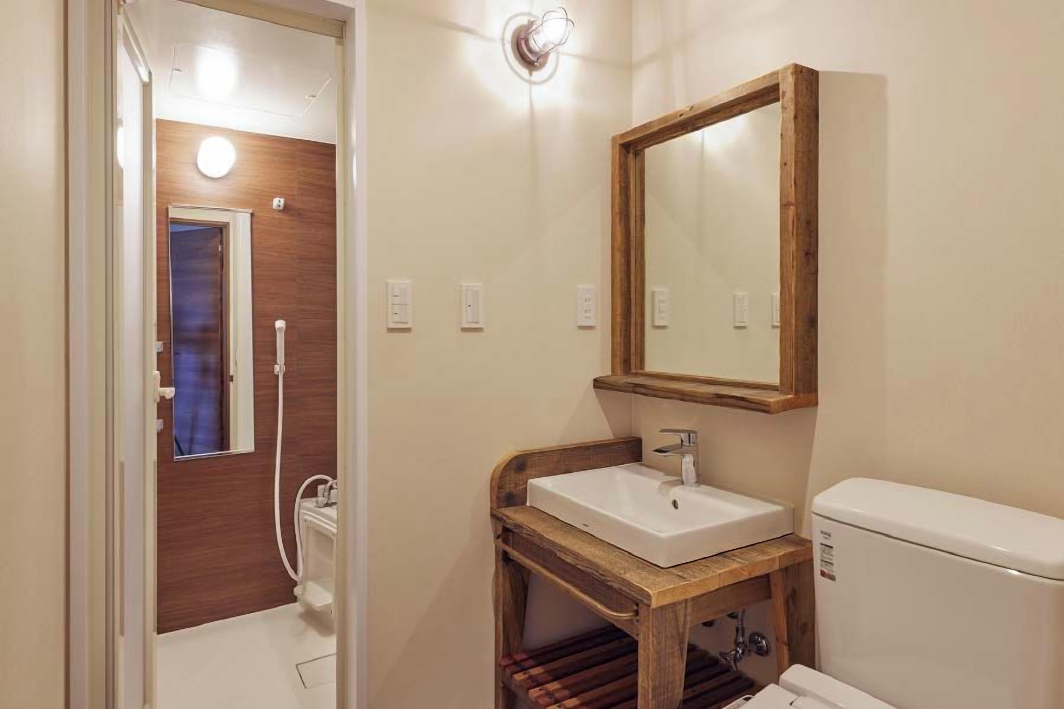 A bathroom with a wooden vanity, a mirror, a toilet, and a shower area.