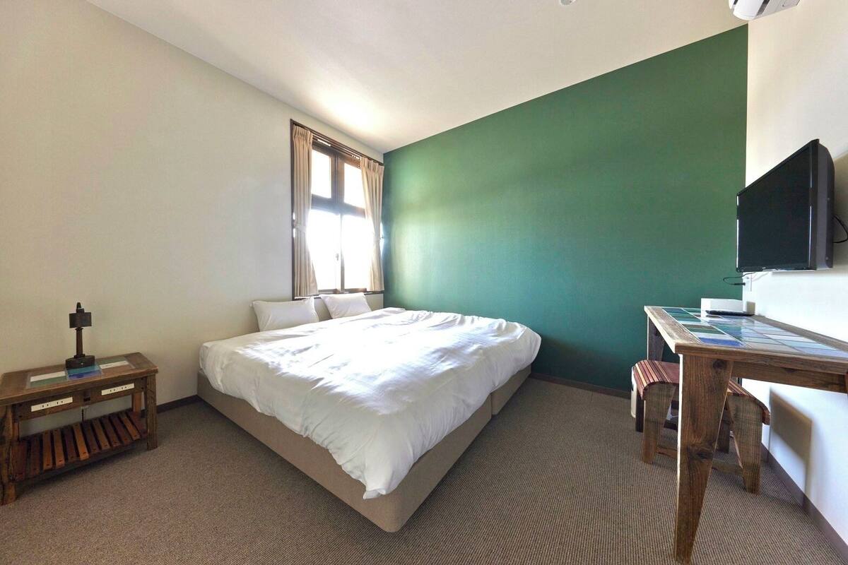 A hotel room with a bed, a desk, a chair, a television, and a window with curtains.