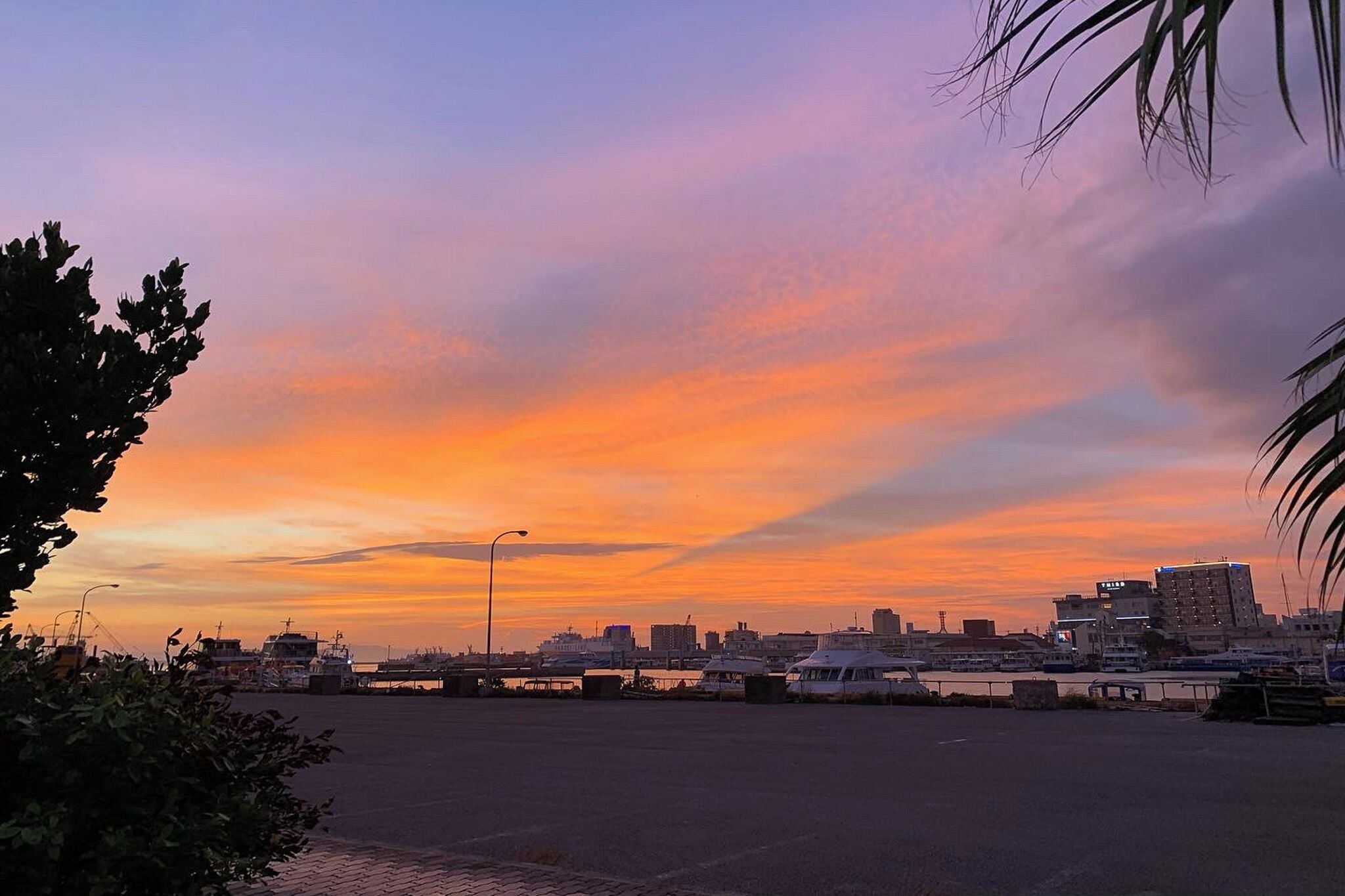 A waterfront cityscape at sunset with buildings, a bridge, and boats.