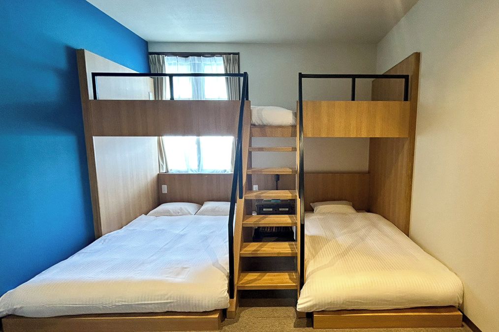 Une chambre avec un lit superposé, un mur bleu, une fenêtre avec des rideaux et une échelle en bois.