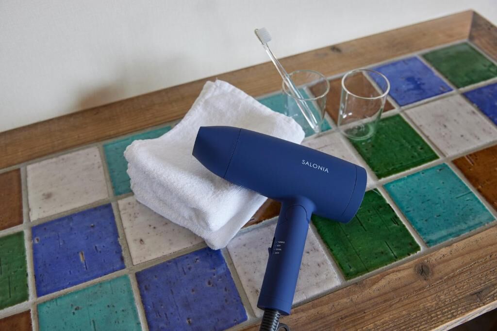 Un sèche-cheveux bleu est posé sur un plateau en bois, accompagné d’un linge blanc et d’un verre.