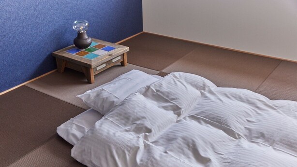 A tatami mat room with a bed and a small table with a decorative item.