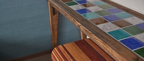 A wooden table with a colorful tile top, a matching wooden stool, and a blue wall in the background.