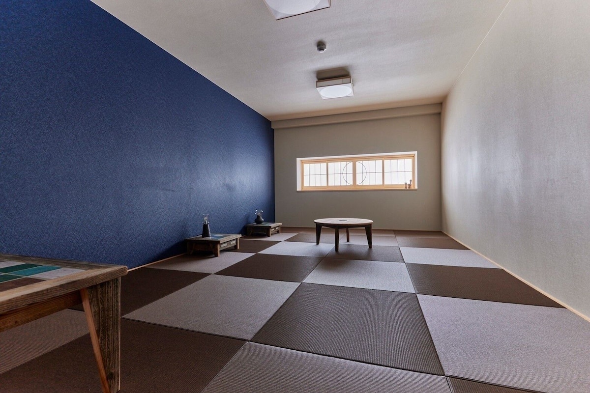 A room with tatami mats, a small table, a window, and a blue wall.