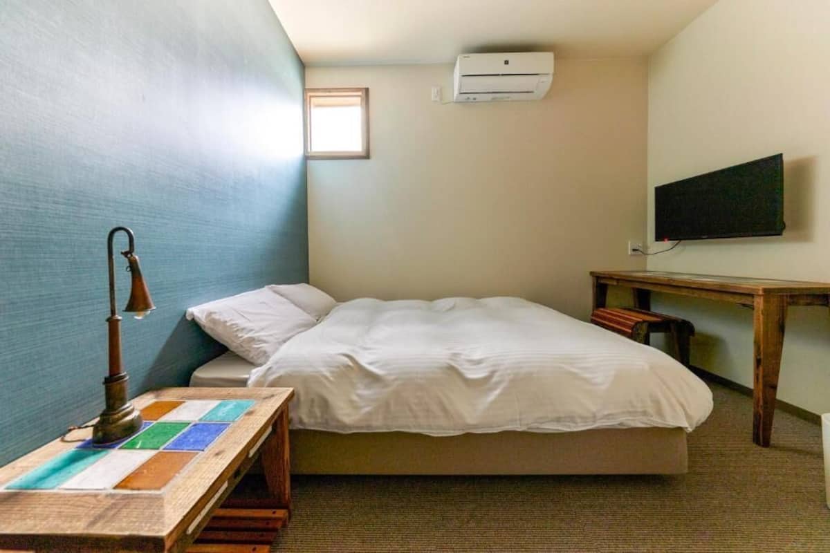 A small, single-bed room with a desk, a wall-mounted TV, and an air conditioning unit.