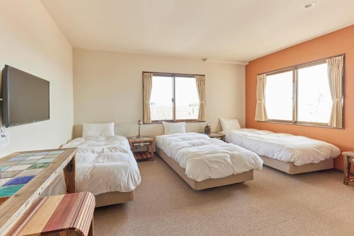 A hotel room with three beds, a flat-screen TV, and large windows.