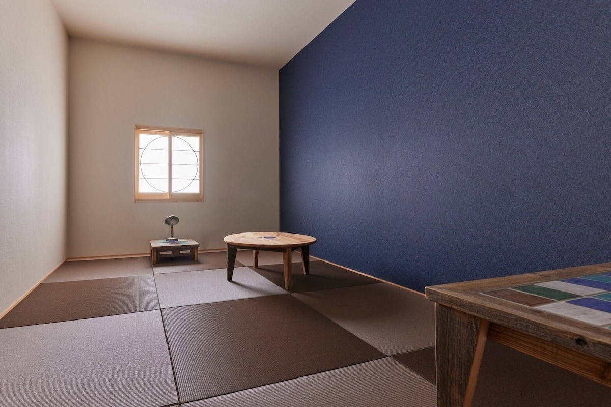 A room with tatami mats, a small table, a stool, and a window with a view.