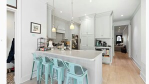 Een moderne keuken met witte kastjes, een centraal eiland met barkrukken, hanglampen en een zichtbare koffiemachine.