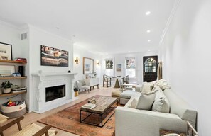 A spacious living room with a fireplace, a sofa, a coffee table, and a dining area with a staircase. - Charming family-friendly rowhome with garage near Center City Philly (Philadelphia)