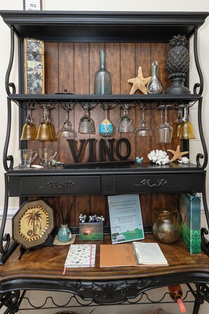 Uma prateleira de madeira exibe diversos objetos de vidro, uma estrela-do-mar, uma abacaxi e uma placa com a inscrição 'VINO'.