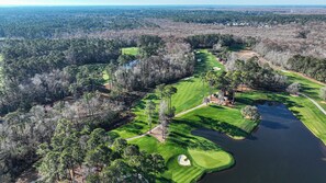 Vista aérea de um campo de golfe com um lago, rodeado por florestas densas e áreas residenciais.
