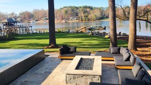 An outdoor seating area with stone flooring, modern sofas, and a fire pit. - Luxury Lake Norman Home (Mooresville)