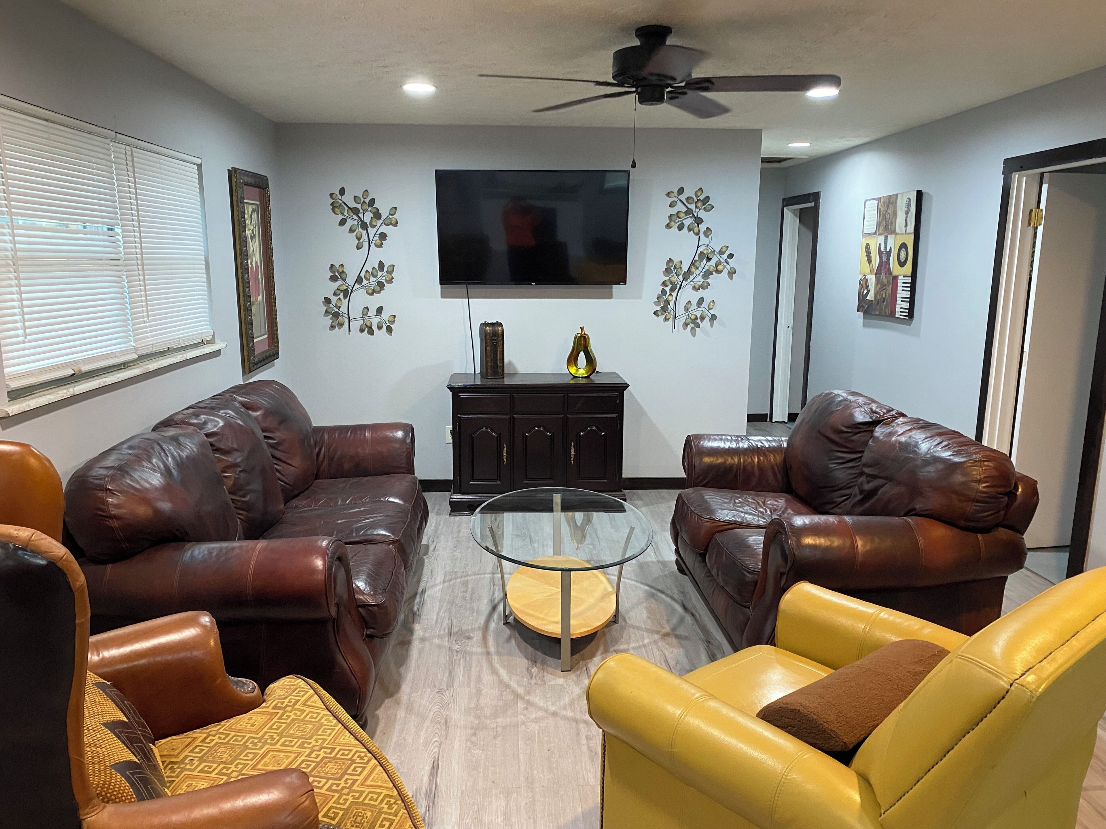 A living room with two brown leather sofas, a yellow armchair, a glass coffee table, and a dark wooden cabinet.