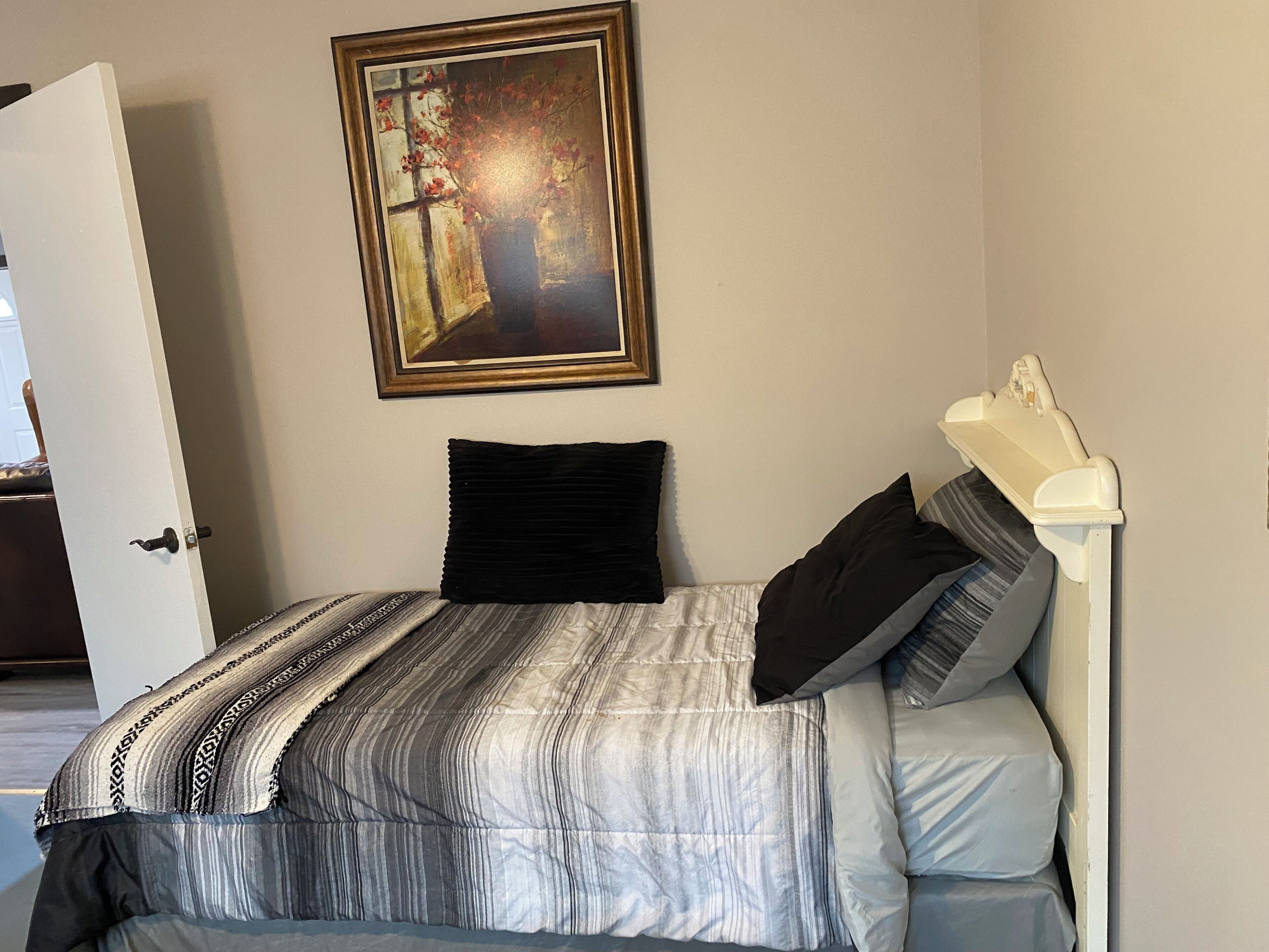 A hotel room with a bed, a painting on the wall, and a white door.