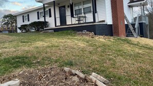 A single-story house with a covered porch, a brick chimney, and a small front yard with a fire pit. - Cozy 3-bedroom house in delightful LaFollette with AC (LaFollette)