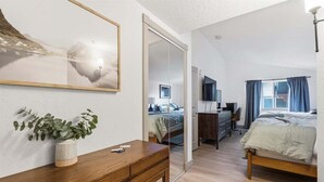 A modern bedroom with a wooden desk, a bed, a TV, and a large window with curtains.