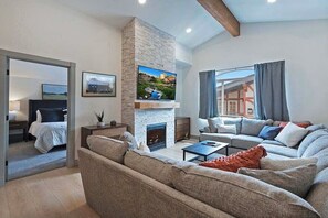 Een moderne woonkamer met een stenen openhaard, een grote flatscreen televisie, een zithoek en een eethoek.