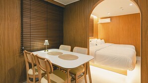 Habitación de hotel moderna con pared de madera, cama con ropa de cama blanca, mesa de comedor con sillas y una lámpara.