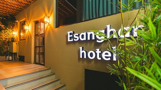 Exterior del hotel Esang, con un cartel, escalones que conducen a la entrada e iluminación exterior.